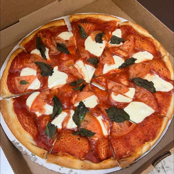 A freshly baked Margherita pizza with rich red sauce, mozzarella, basil, and sliced tomatoes in a box.