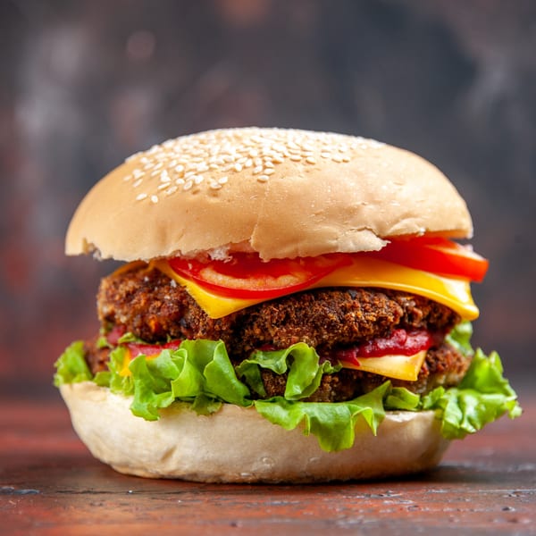 A close-up of a double-patty burger with cheese, lettuce, and tomato on a sesame seed bun.