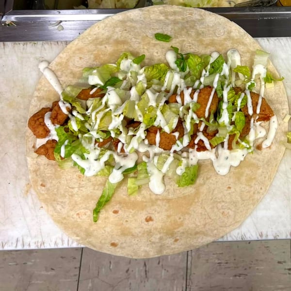 A tortilla filled with crispy chicken, fresh lettuce, and drizzled with creamy white sauce.