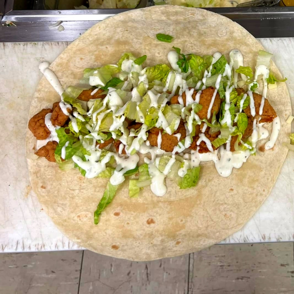 A tortilla filled with crispy chicken, fresh lettuce, and drizzled with creamy white sauce.