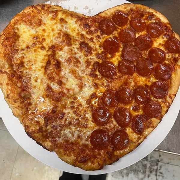 Heart-shaped pizza, half cheese and half pepperoni, on a white paper plate.